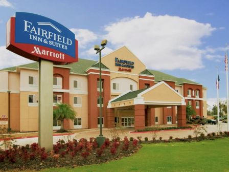 The image shows a Fairfield Inn & Suites by Marriott hotel building with a large sign, well-maintained landscaping, and three flagpoles.