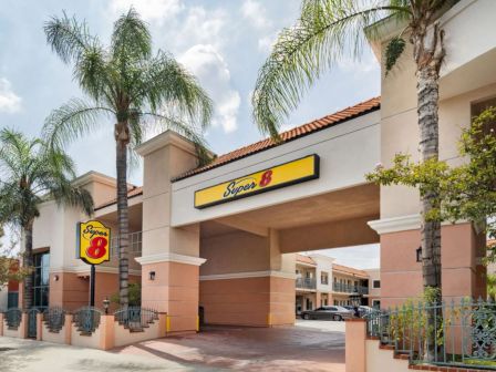 The image shows an entrance of a Super 8 hotel, flanked by palm trees and featuring a yellow sign with the hotel logo.