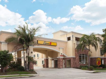 This image shows a Super 8 motel building with palm trees in front, featuring a prominent sign and a clear, blue sky with scattered clouds.